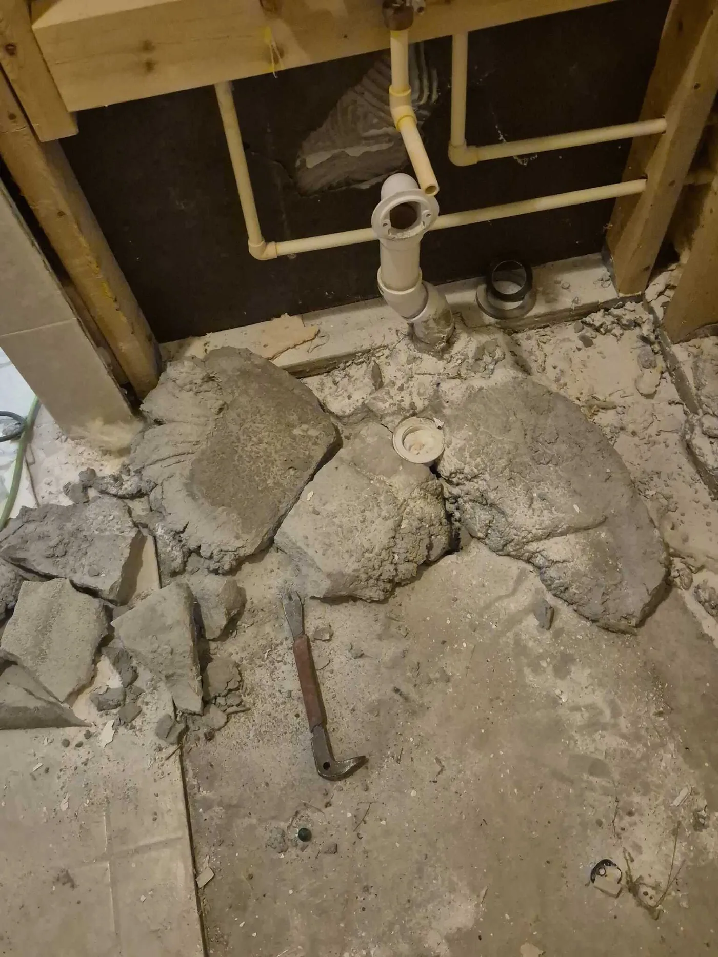 Bathroom stripped to the slab with the concrete floor broken out and new rough-in drain and supply lines set between studs.